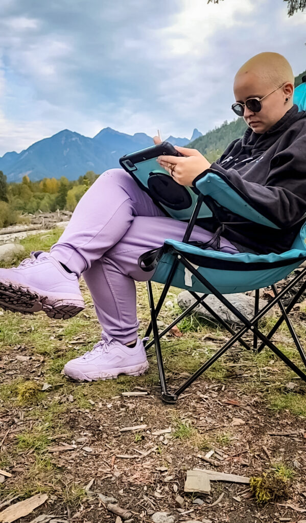 a person sitting on a chair drawing on a tablet in the mountains